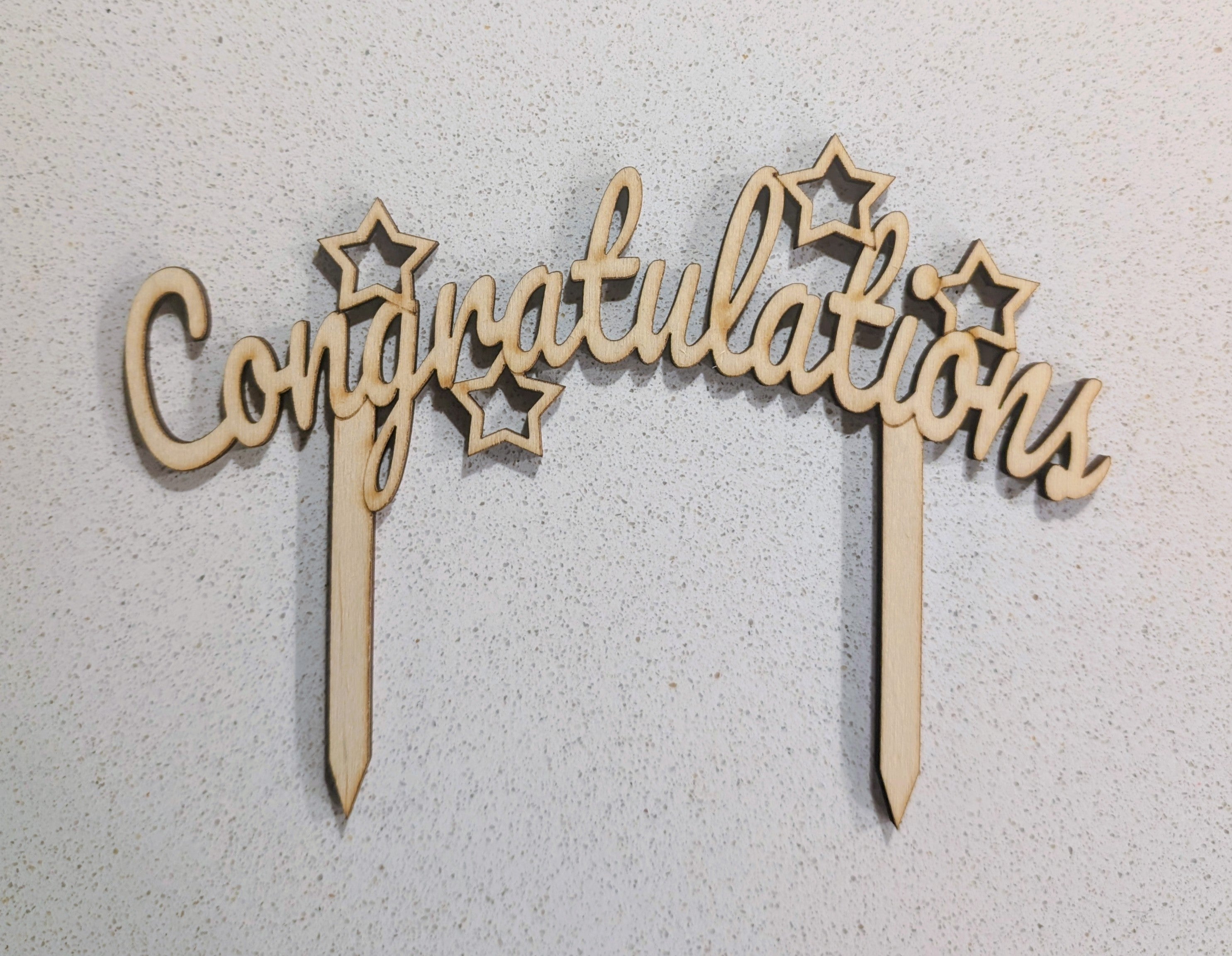Wooden 'Congratulations' cake topper with stars on a light gray background, available to buy at Beardy Baker.