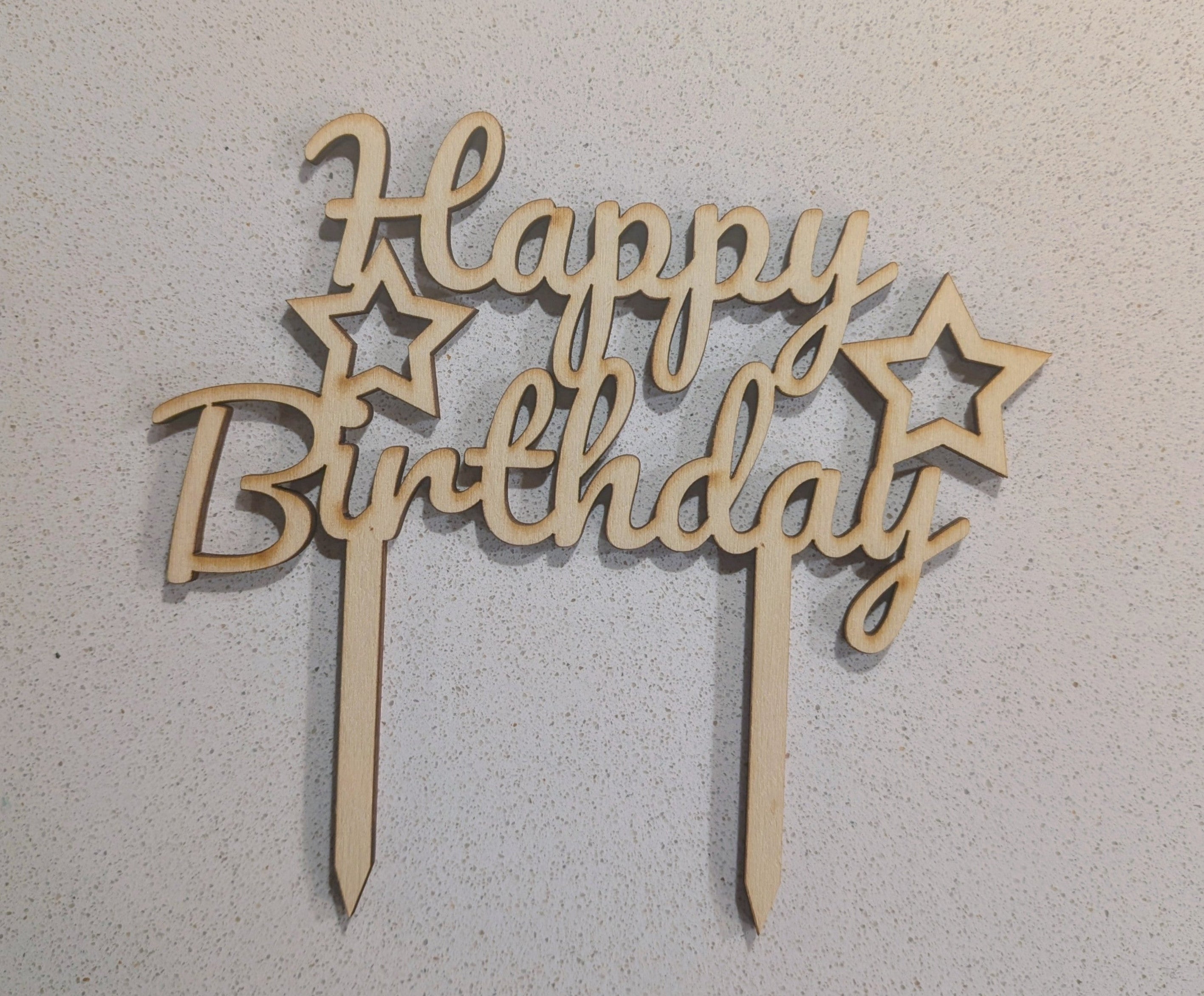 Wooden 'Happy Birthday' cake topper with stars on a light grey background, available to buy at Beardy Baker.